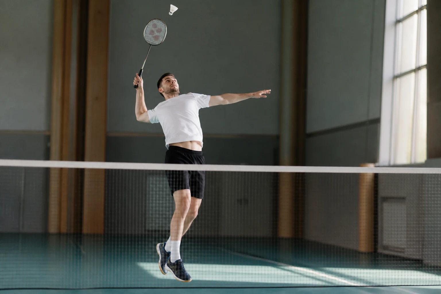 Joueur de badminton frappant un volant avec sa raquette près du filet