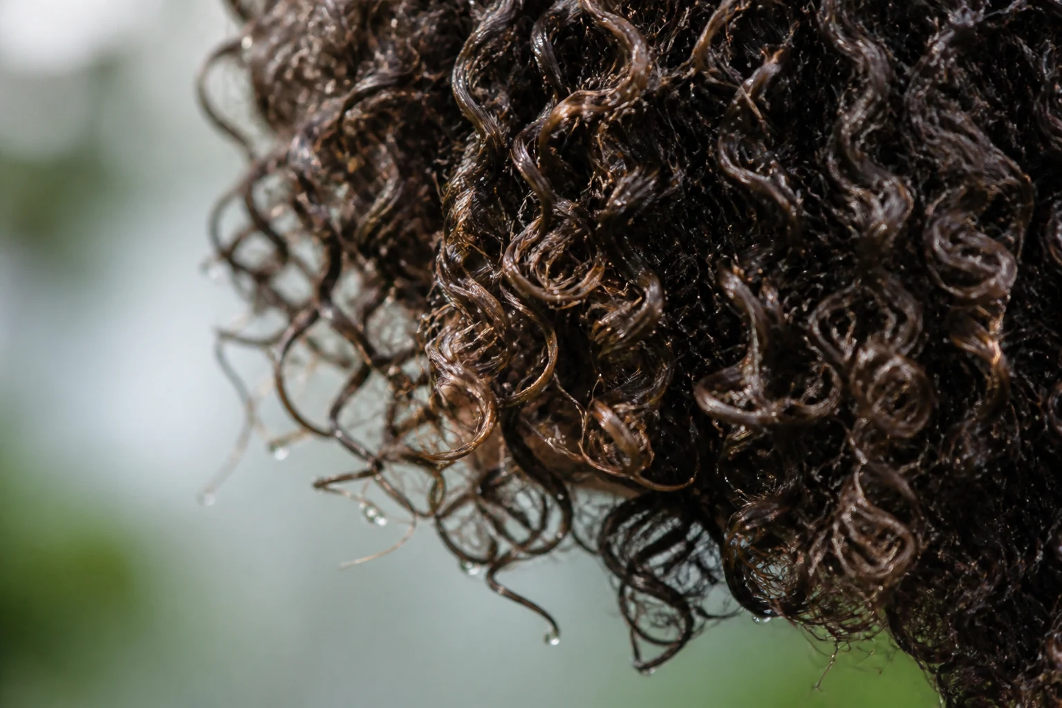 Femme aux cheveux bouclés appliquant la méthode curly girl devant un miroir