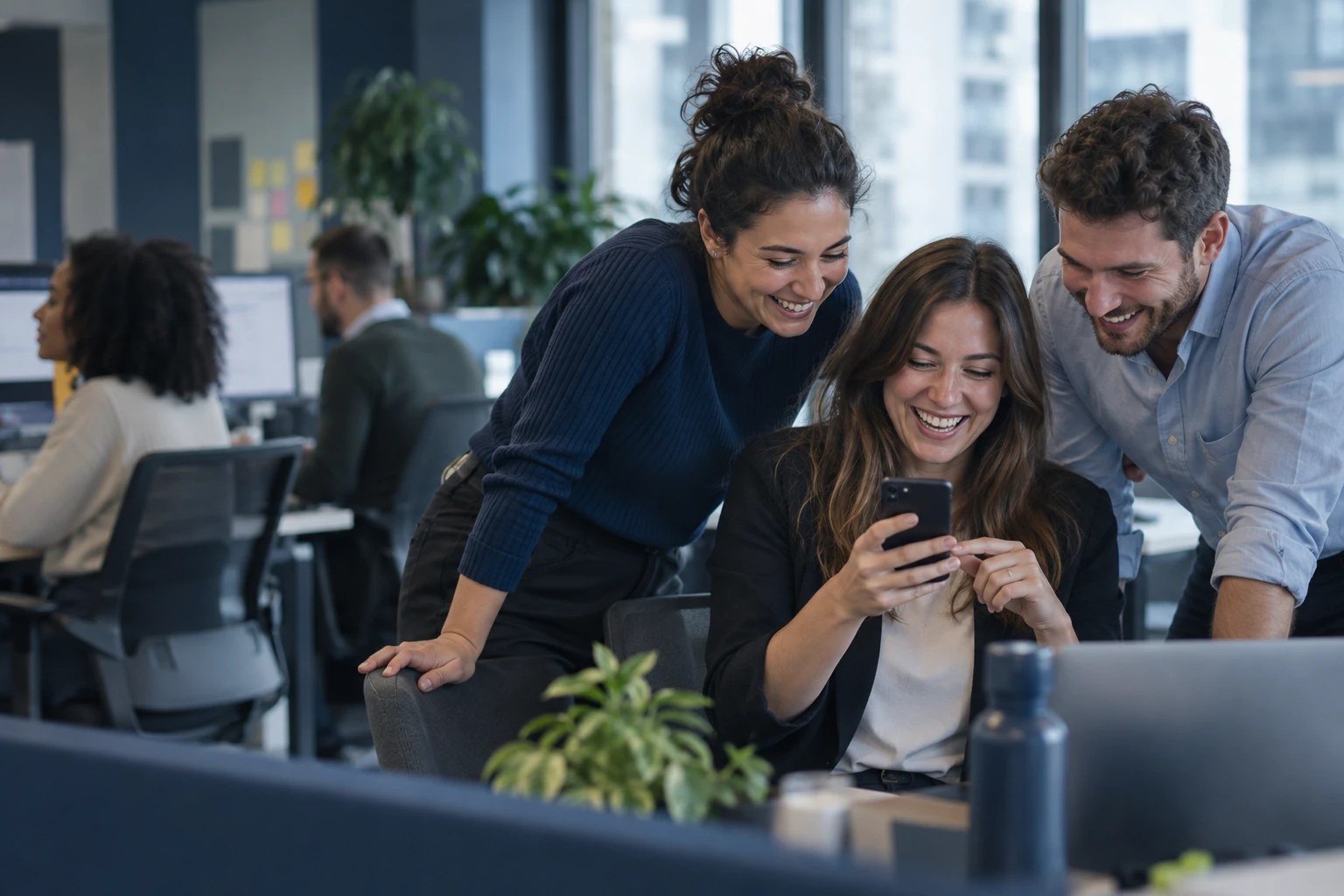 Collègues riant en lisant un message sur un smartphone dans un open space